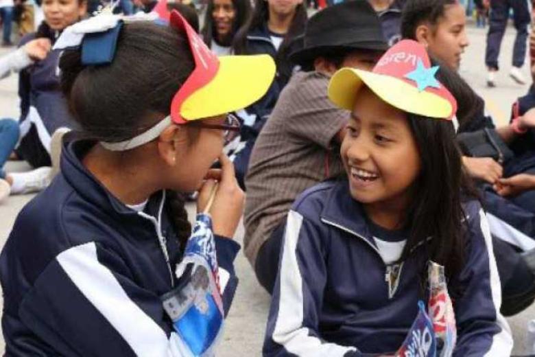 Two girls wearing yellow-billed hats in conversations among other children groups in the background