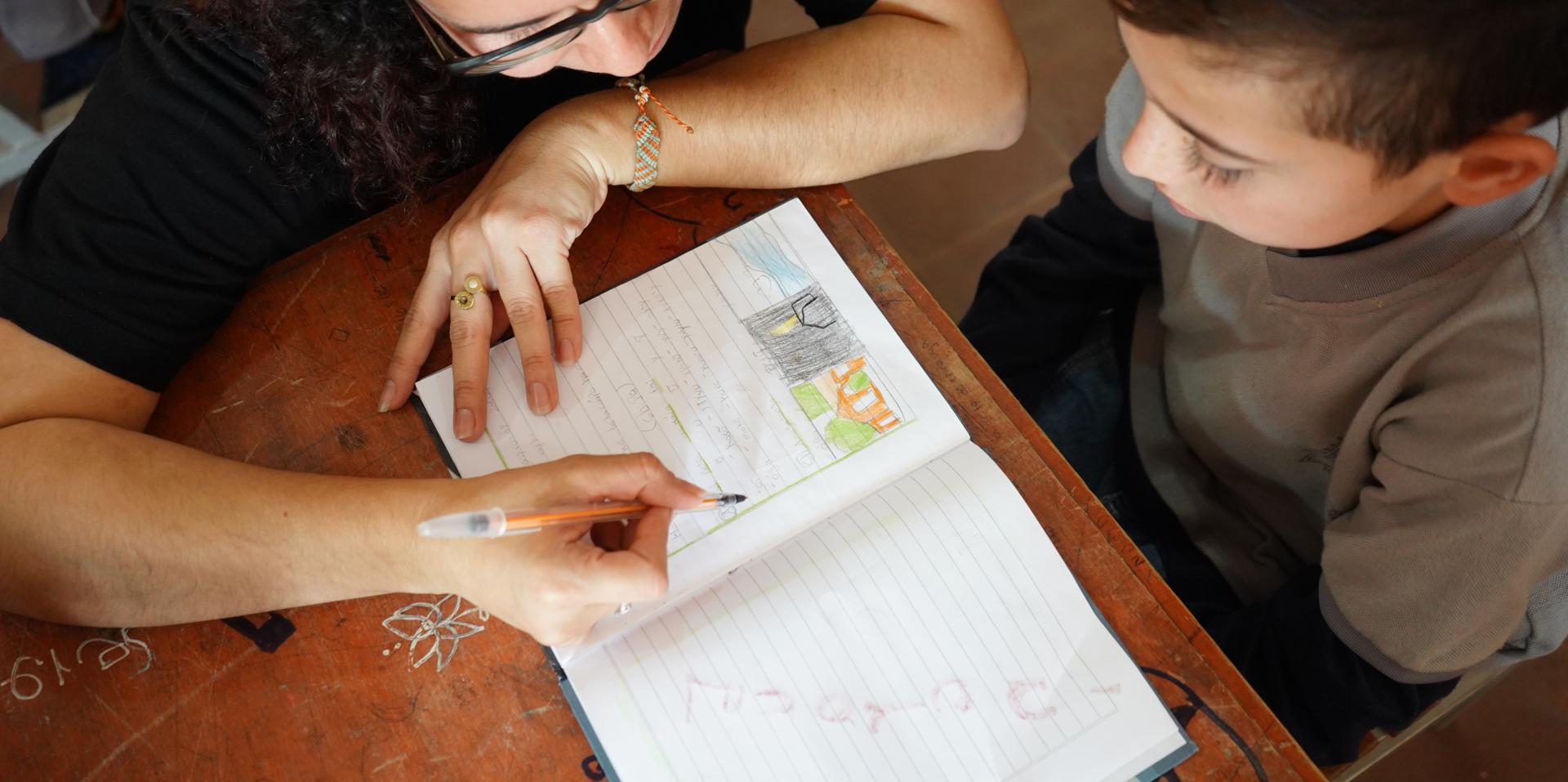 Overhead shot of a teacher and young boy reviewing an entry in a notebook together