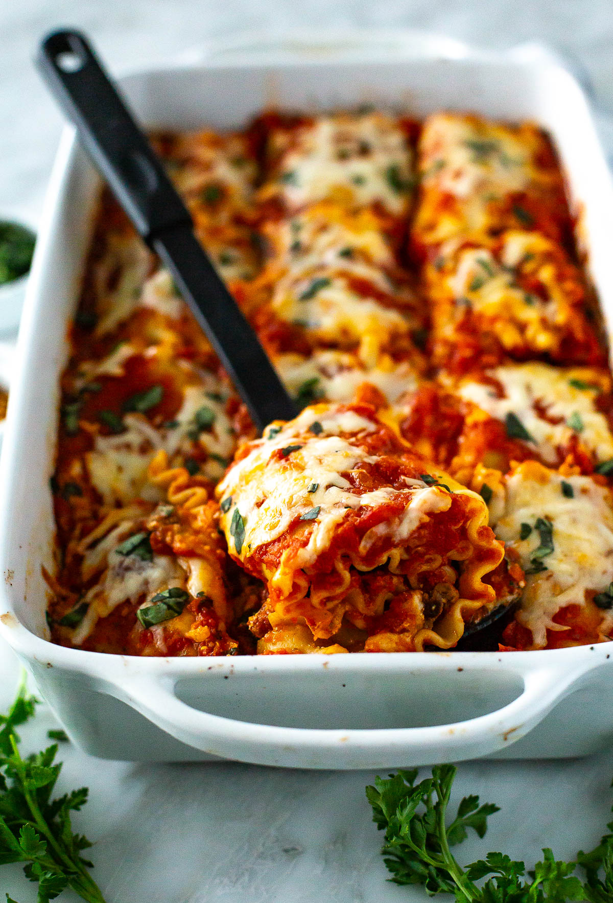 Close up of lasagna roll-ups fresh out of the oven, one piece lifted by spatula