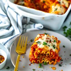 A plate of cheesy spinach lasagna roll-ups topped with melted mozzarella cheese and garnished with fresh basil.