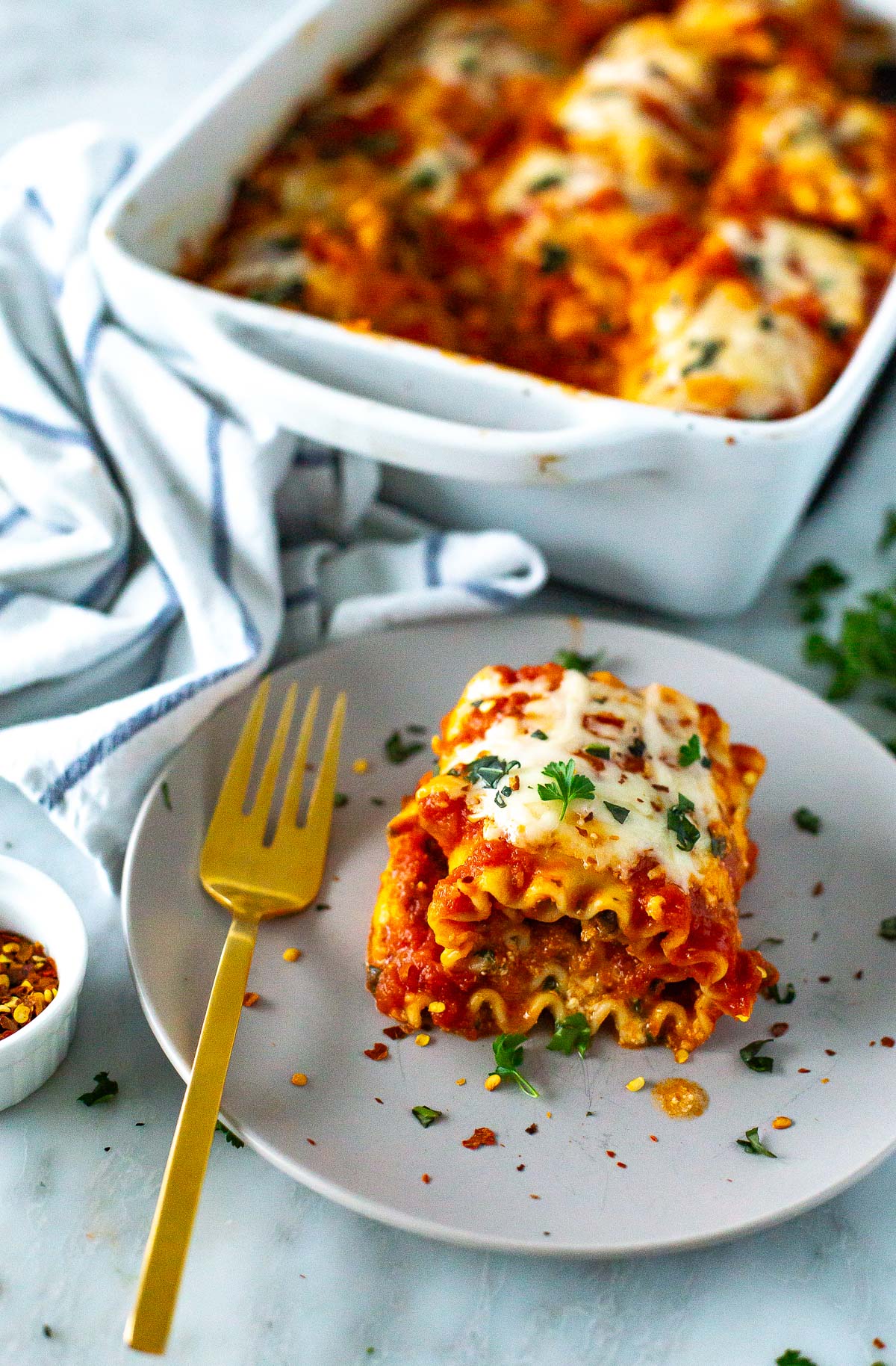 A plate of cheesy spinach lasagna roll-ups topped with melted mozzarella cheese and garnished with fresh basil.
