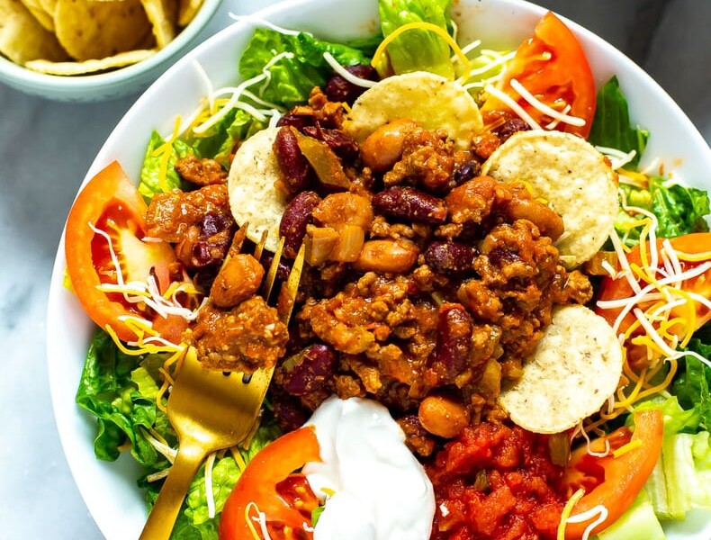 A bowl of Copycat Wendy's Taco Salad with tortilla chips and shredded cheese in small bowls on the side.